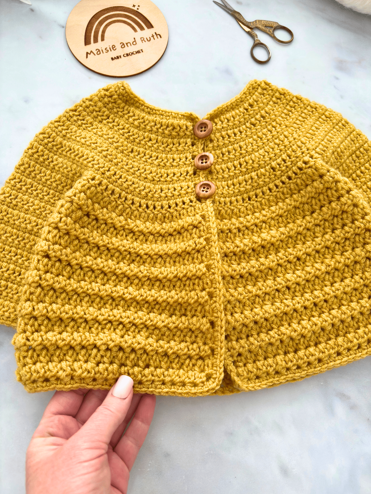 Crochet baby cardigan pattern with textured stitch design in mustard yellow yarn